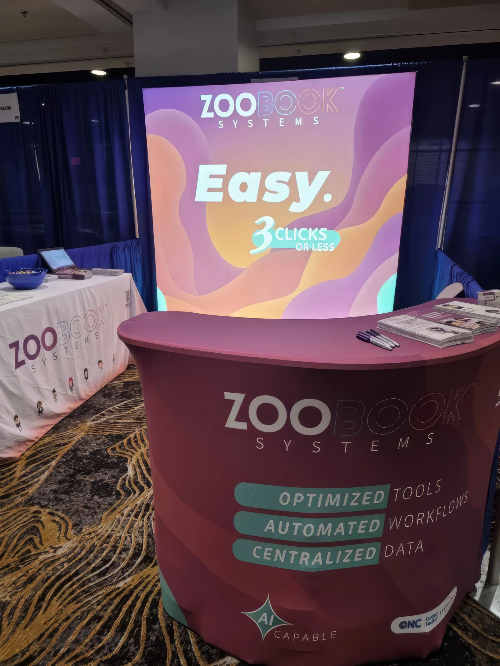Zoobook Systems conference booth — Easy. 3 Clicks or Less. Optimized Tools, Automated Workflows, Centralized Data. AI Capable. ONC Certified.